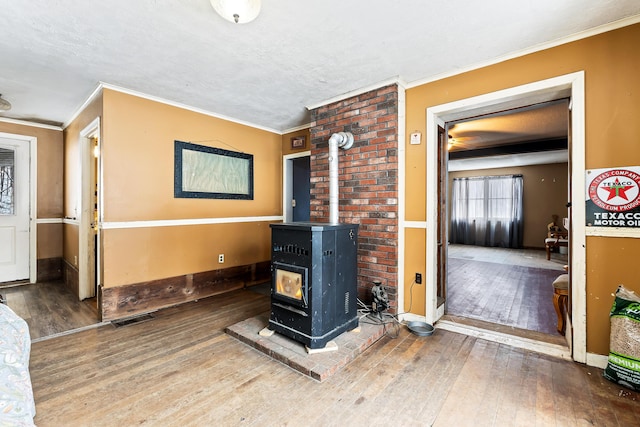 interior space featuring a wood stove, wood-type flooring, baseboards, visible vents, and ornamental molding