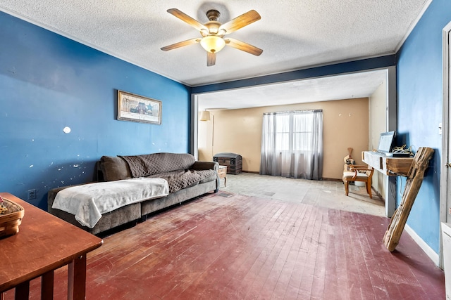 living area featuring a textured ceiling, wood-type flooring, baseboards, and a ceiling fan