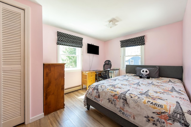 bedroom with a baseboard radiator, wood finished floors, a closet, and baseboards