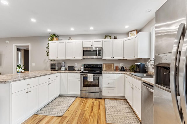 kitchen with a sink, a peninsula, light wood-type flooring, stainless steel appliances, and white cabinets