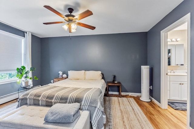 bedroom featuring a sink, a ceiling fan, ensuite bath, baseboards, and light wood-style floors