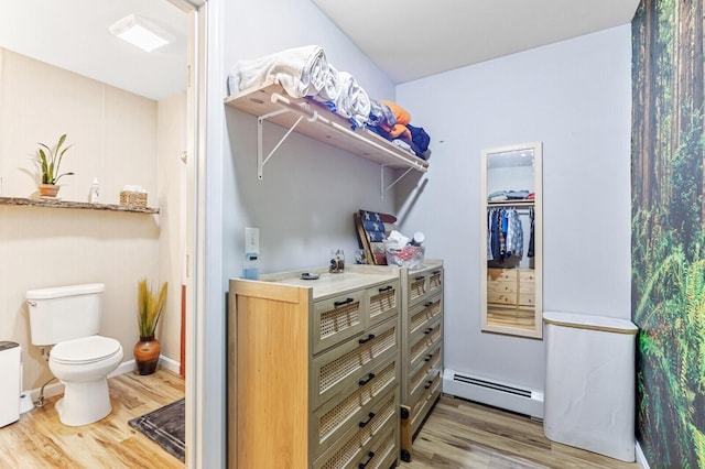 bathroom with baseboards, wood finished floors, a baseboard heating unit, and toilet