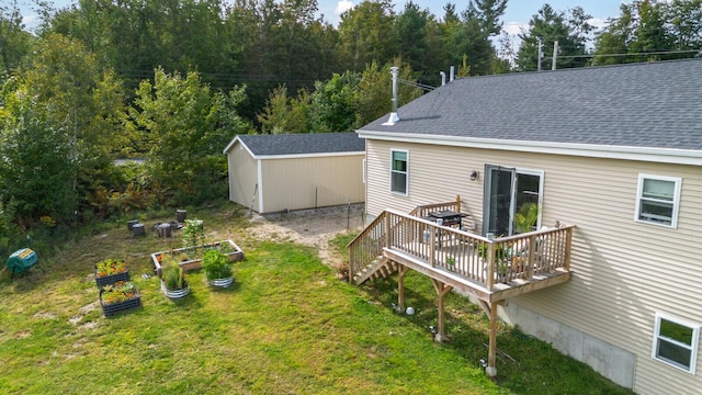 rear view of house with an outbuilding, a storage unit, a garden, a shingled roof, and a yard