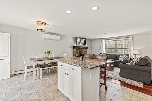 kitchen featuring a kitchen island, open floor plan, a breakfast bar area, a wall unit AC, and white cabinets