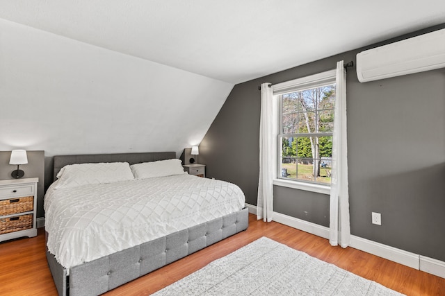 bedroom with baseboards, a wall mounted AC, vaulted ceiling, and wood finished floors
