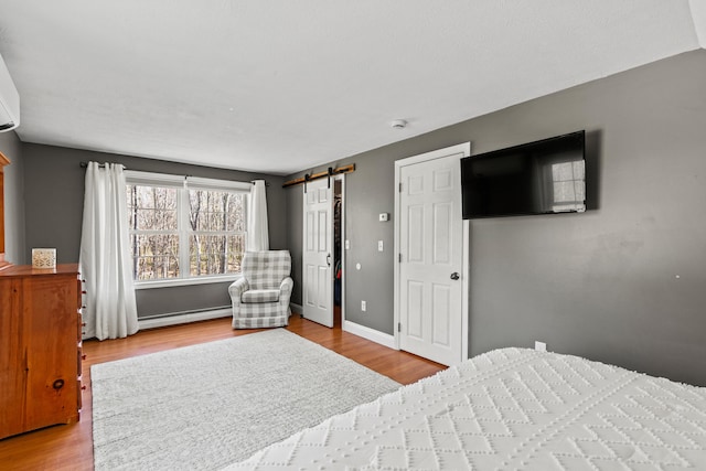 bedroom with wood finished floors, a barn door, baseboards, and a baseboard heating unit