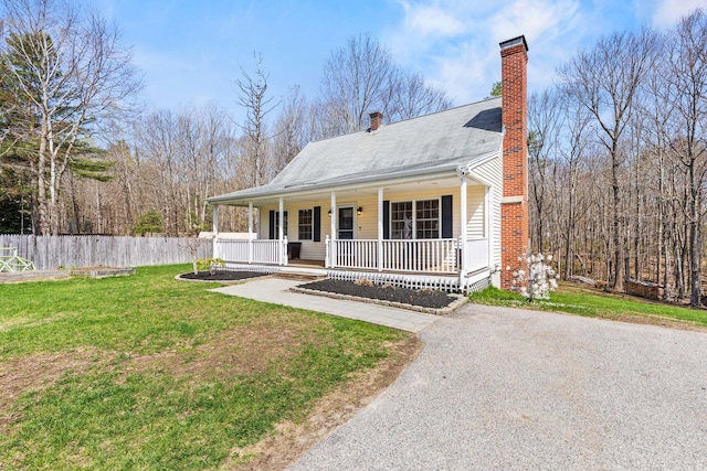 view of front of home featuring covered porch, a chimney, a front yard, fence, and aphalt driveway