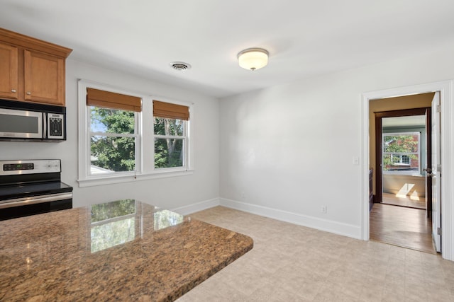 23-25 Deerfield Rd, Portland, ME 04101 - kitchen featuring appliances with stainless steel finishes, brown cabinetry, dark stone counters, baseboards, and light flooring