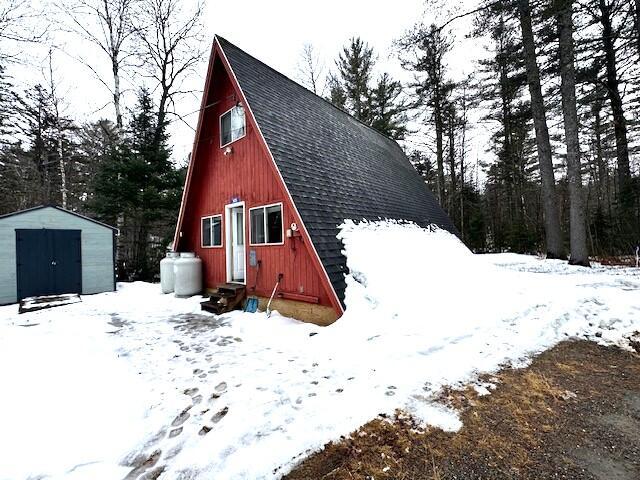 snow covered structure with an outdoor structure, entry steps, and a shed
