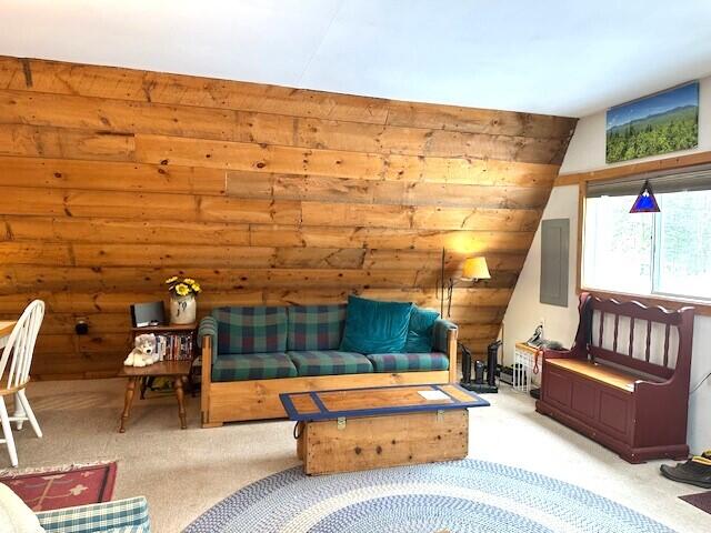 carpeted living room featuring vaulted ceiling, electric panel, and wooden walls