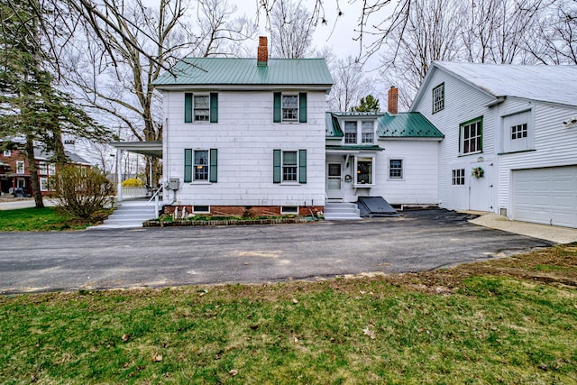 back of property featuring metal roof, driveway, covered porch, a garage, and a chimney