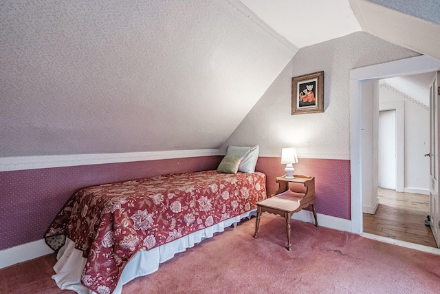 carpeted bedroom featuring baseboards, wallpapered walls, a textured ceiling, and vaulted ceiling