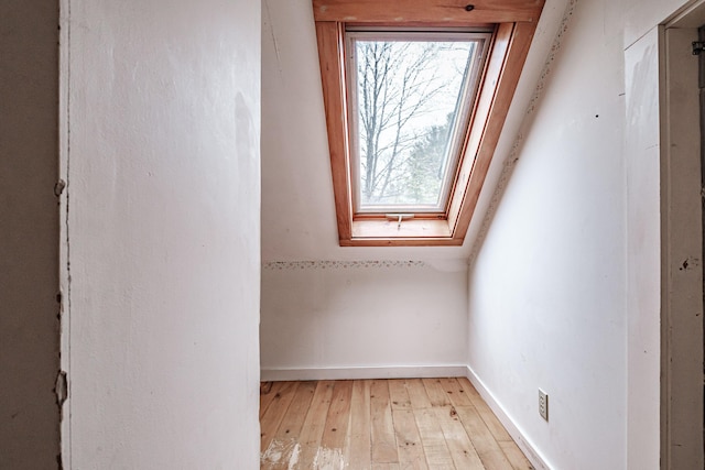 interior space featuring baseboards, light wood-style flooring, and vaulted ceiling with skylight
