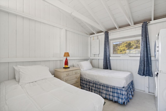 bedroom with concrete flooring, stacked washer / drying machine, and vaulted ceiling with beams