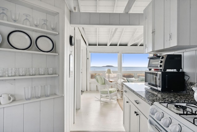 kitchen featuring open shelves, white range with gas stovetop, a water view, white cabinets, and stone counters