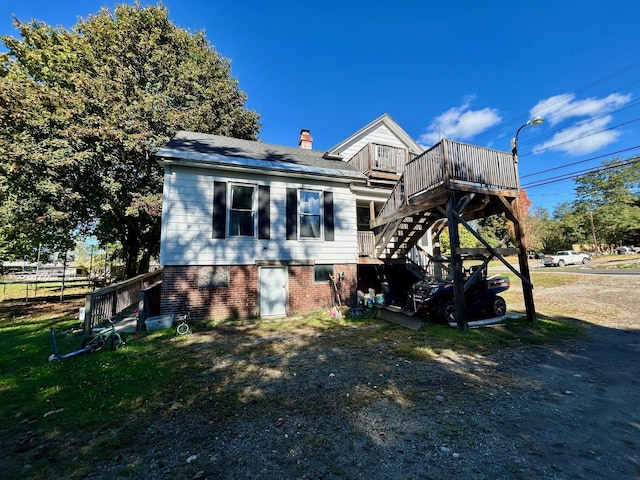 view of home's exterior with a shingled roof, a deck, a chimney, stairway, and brick siding