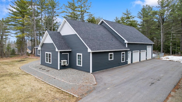 view of front of house featuring a front yard, an attached garage, driveway, and a shingled roof