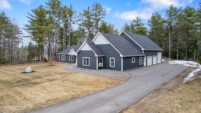 view of front of house with roof with shingles, a fire pit, driveway, a front lawn, and a garage