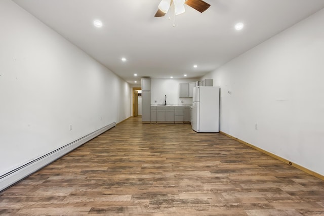 unfurnished living room featuring ceiling fan, recessed lighting, wood finished floors, a baseboard heating unit, and a sink