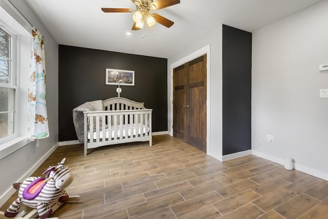unfurnished bedroom featuring a closet, baseboards, a ceiling fan, a crib, and wood finish floors