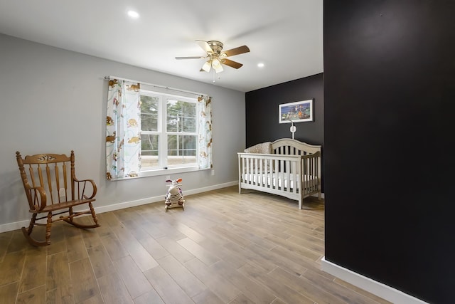 bedroom with baseboards, a crib, recessed lighting, ceiling fan, and wood finished floors