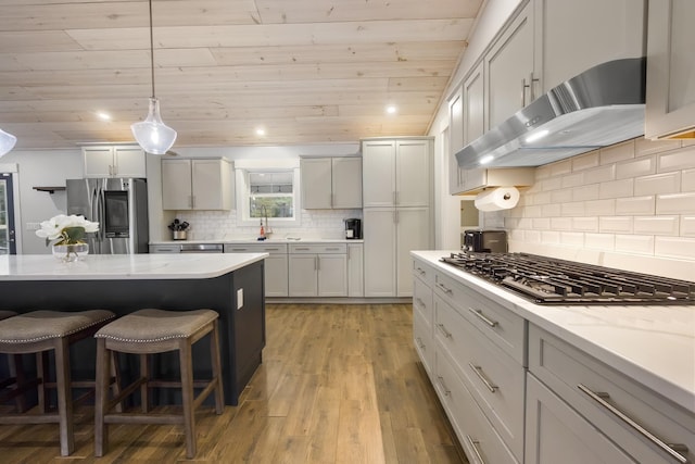 kitchen with stainless steel fridge, a breakfast bar, wood ceiling, under cabinet range hood, and gas cooktop