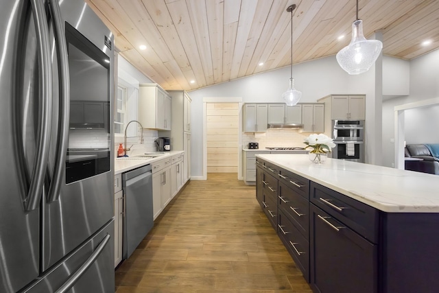 kitchen with tasteful backsplash, under cabinet range hood, lofted ceiling, stainless steel appliances, and a sink