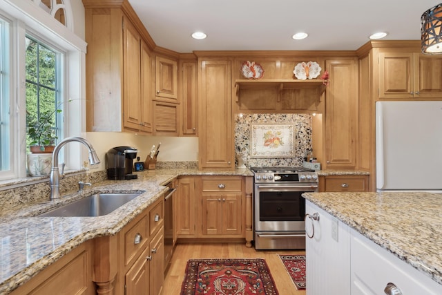 kitchen featuring recessed lighting, light stone counters, a sink, light wood-style flooring, and appliances with stainless steel finishes