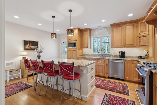 kitchen with a kitchen breakfast bar, a kitchen island, a sink, stainless steel appliances, and light wood-style flooring