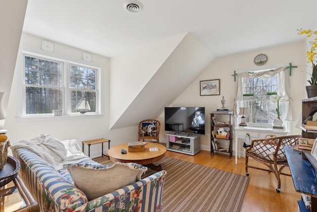 living area featuring visible vents, lofted ceiling, wood finished floors, and a healthy amount of sunlight