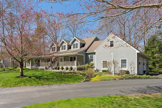 new england style home with a porch, an attached garage, and a front yard