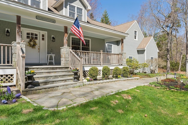 entrance to property featuring roof with shingles, a lawn, and a porch
