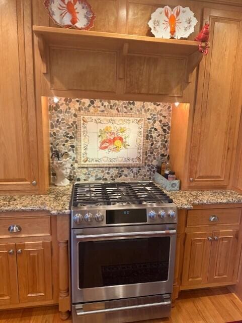 kitchen with light wood-style floors, decorative backsplash, light stone countertops, and stainless steel range with gas cooktop