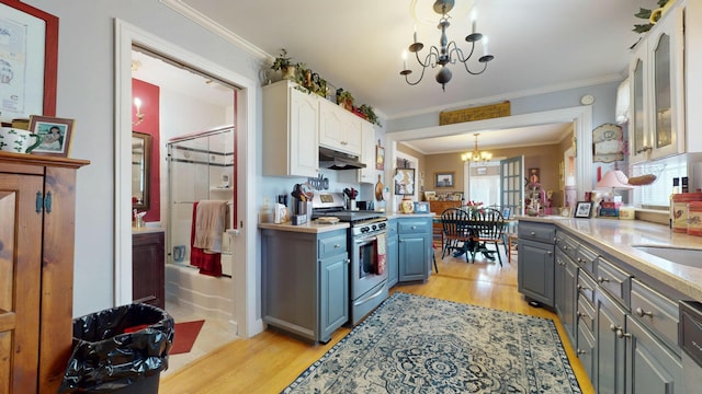 150 Enfield Rd, Lincoln, ME 04457 - kitchen with a notable chandelier, gas range, under cabinet range hood, light wood finished floors, and gray cabinetry