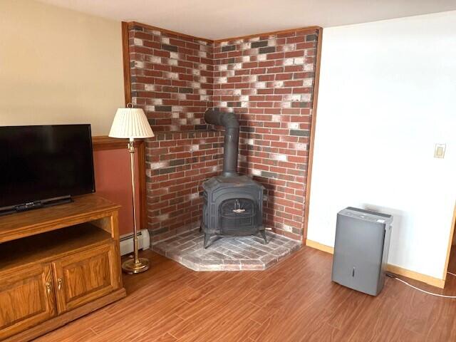 160 Pinkhams Cove Rd, Belgrade, ME 04917 - unfurnished living room with a wood stove, baseboards, light wood finished floors, and a baseboard radiator