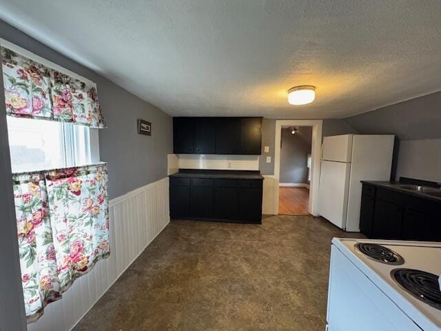 kitchen featuring lofted ceiling, wainscoting, white appliances, and a textured ceiling