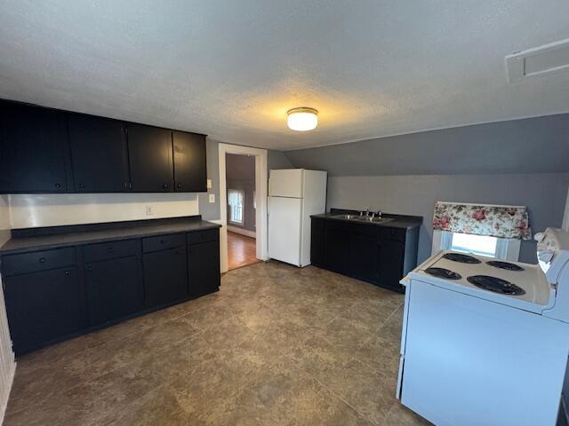 kitchen featuring a sink, a textured ceiling, dark countertops, lofted ceiling, and white appliances