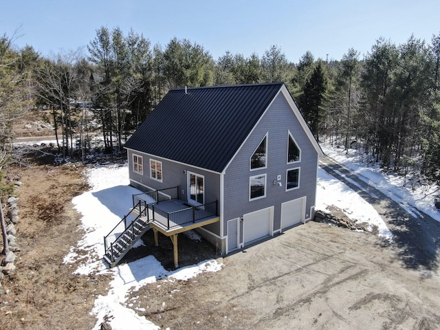 28 First St, Bethel, ME 04217 - snow covered house featuring stairs, dirt driveway, a deck, an attached garage, and metal roof