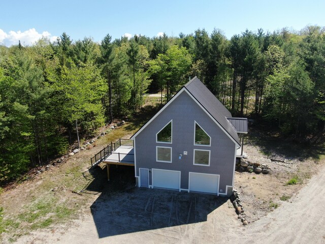 28 First St, Bethel, ME 04217 - exterior space with a forest view, a wooden deck, an attached garage, dirt driveway, and a standing seam roof