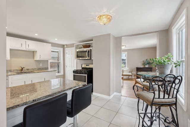 17 E Cove St, Portland, ME 04101 - kitchen with stainless steel appliances, a sink, light tile patterned floors, white cabinets, and light stone counters