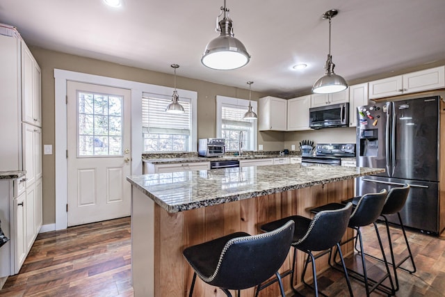 kitchen with appliances with stainless steel finishes, hanging light fixtures, light stone counters, white cabinets, and dark wood-style floors