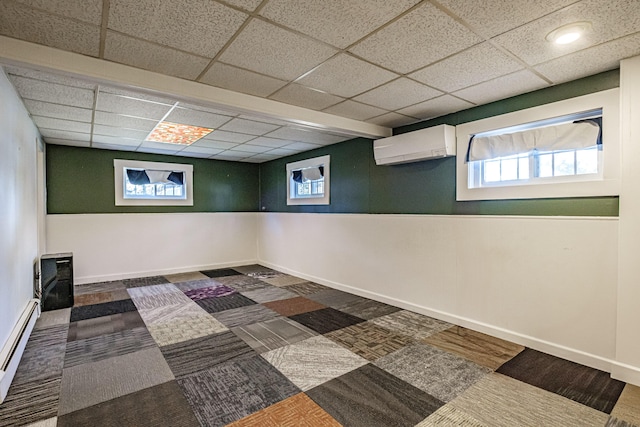 below grade area featuring carpet, baseboards, a drop ceiling, a wall unit AC, and a baseboard radiator