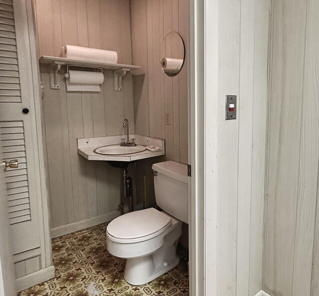 half bathroom featuring wooden walls, baseboards, toilet, and a sink