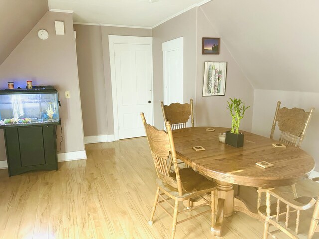 dining area with baseboards, ornamental molding, vaulted ceiling, and light wood finished floors