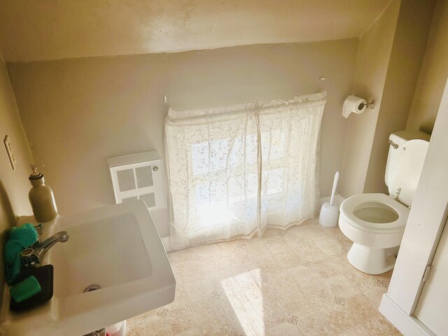 bathroom featuring a bathing tub, toilet, heating unit, and a sink