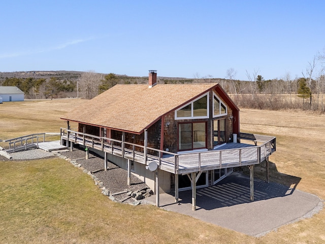 rear view of house featuring a lawn, a shingled roof, and a wooden deck