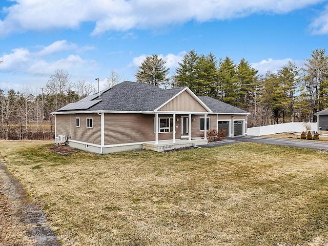 view of front of house featuring covered porch, an attached garage, roof mounted solar panels, a front yard, and aphalt driveway
