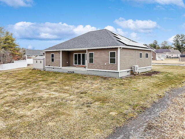back of house featuring a storage shed, a lawn, roof mounted solar panels, fence, and roof with shingles