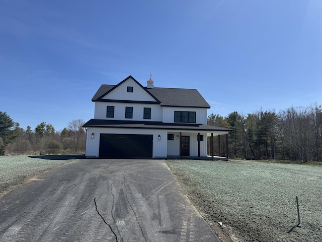 view of front of house with covered porch, aphalt driveway, a chimney, and a garage