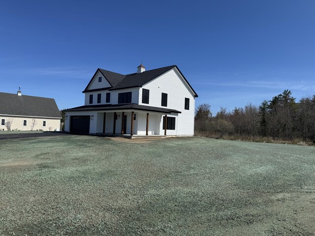 view of front of property featuring a porch, a garage, driveway, and a chimney